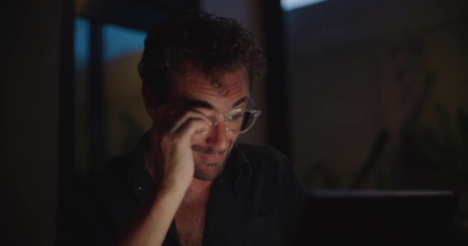 Man taking off and putting on glasses while looking at a laptop