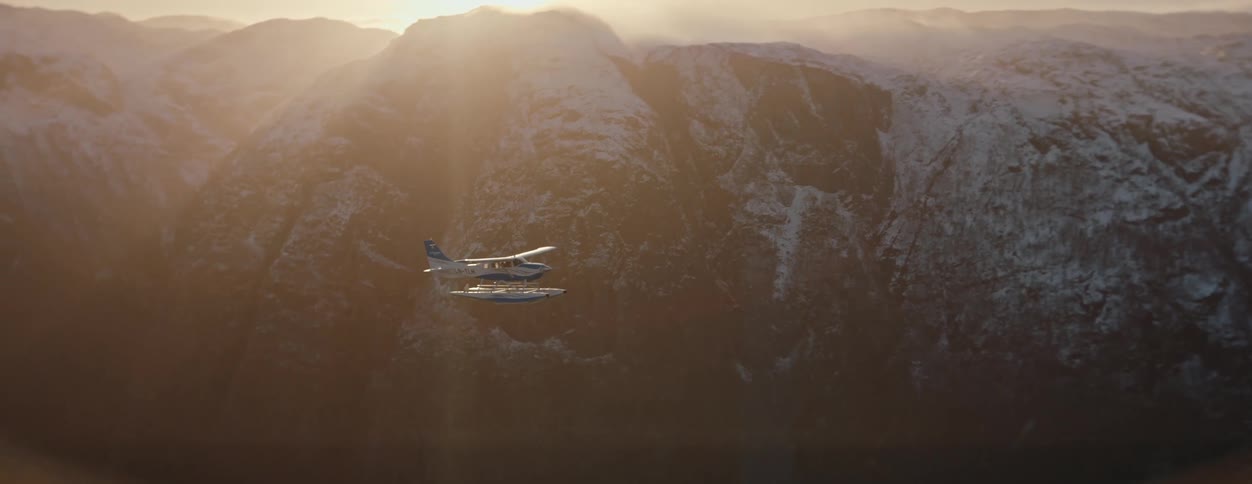 A small plane flies beside a snowcovered mountain range at sunrise