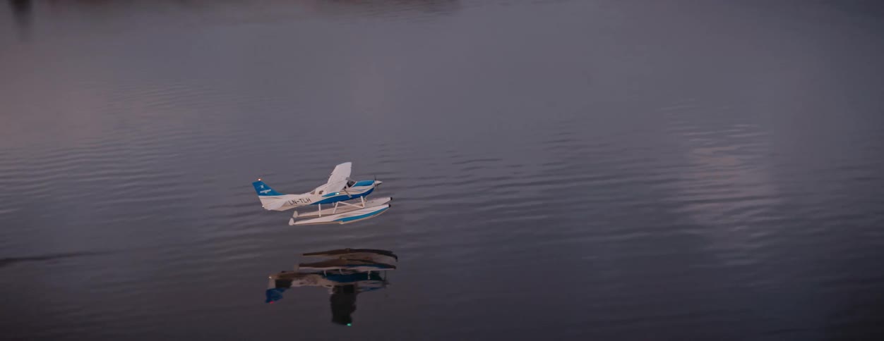 A blue and white seaplane skims the surface of a vast expanse of dark water creating a trailing wake