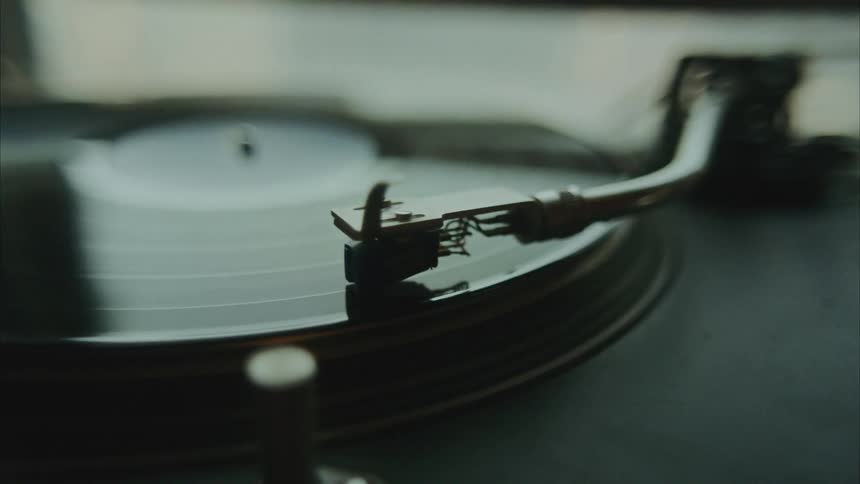 A vintage record players tonearm gently moving across a vinyl record suggesting the playback of music