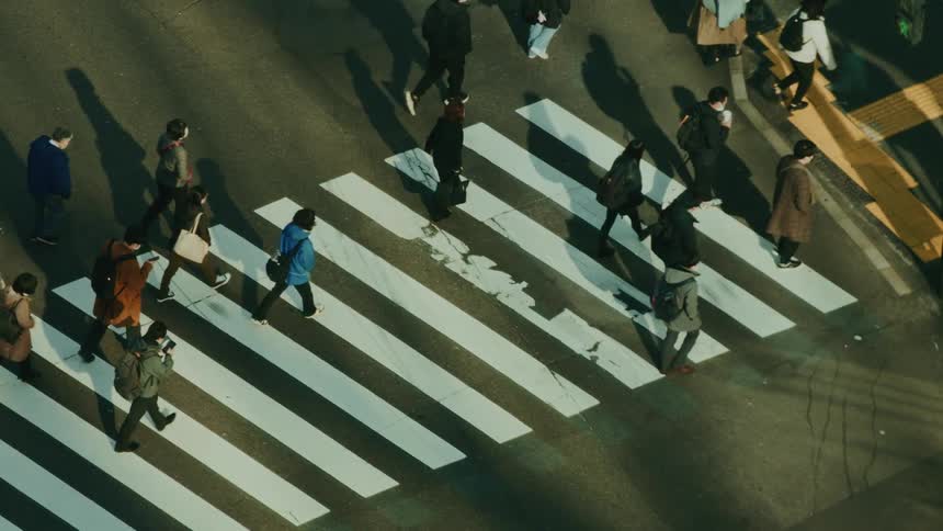 Aerial view of a busy crosswalk with people walking in different directions casting long shadows in the sunlight