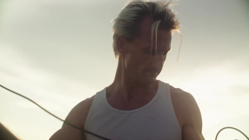 Man in tank top outdoors holding a wire connected to a metal rod