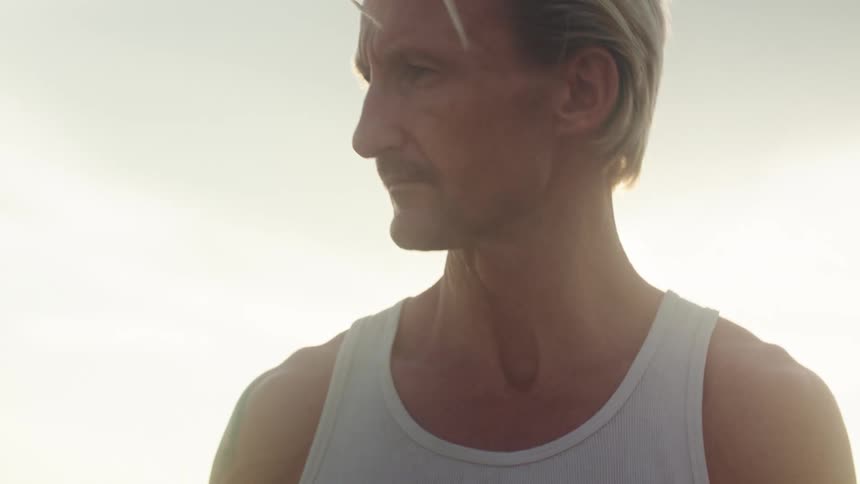 A man in a white tank top appears deep in thought in soft sunlight before handling a bundle of cables outdoors