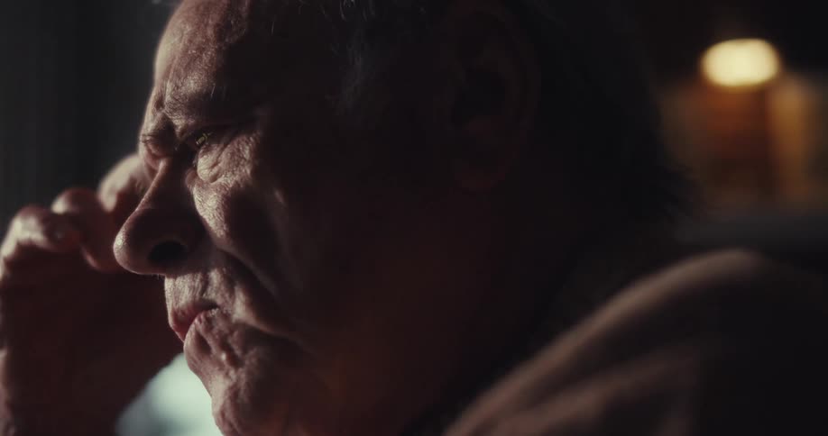 An elderly man sits in a dimly lit room lost in thought as he contemplates and works through his thoughts