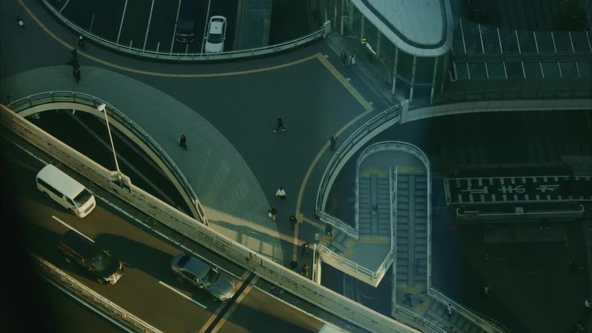An aerial view of a city overpass shows people walking along curved paths and stairways amid surrounding roads