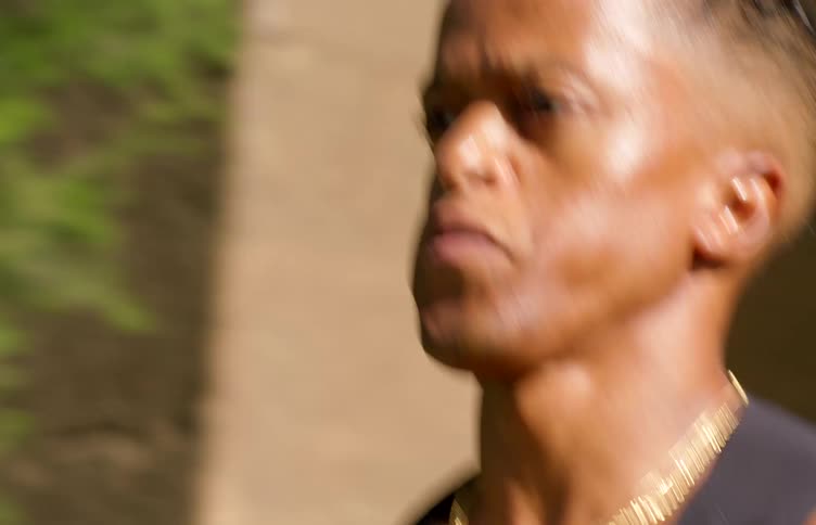 Closeup of a mans face while jogging on a sunny day wearing a black undershirt and a gold chain