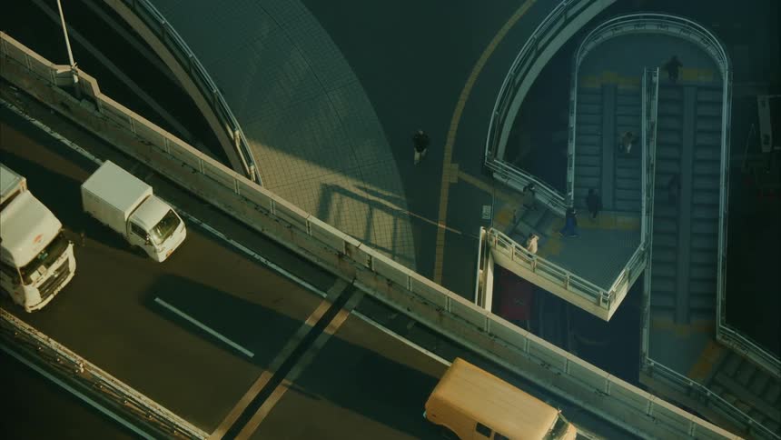 View from above of an overpass with vehicle traffic and pedestrians on the steps through the city in the background