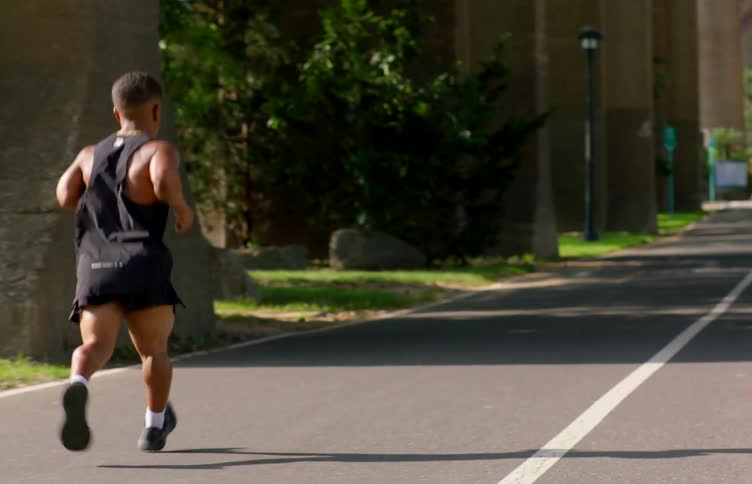 Man in tank top and shorts running down a paved street