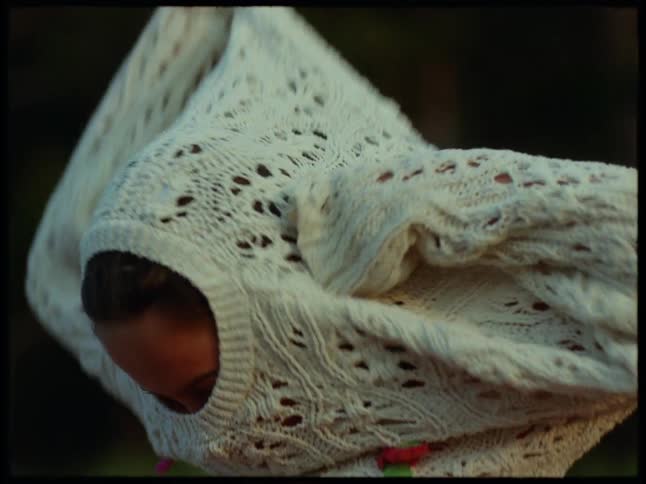 A young woman fresh from a swim pulls on a white crochet knit sweater over her red swimsuit in a serene outdoor setting