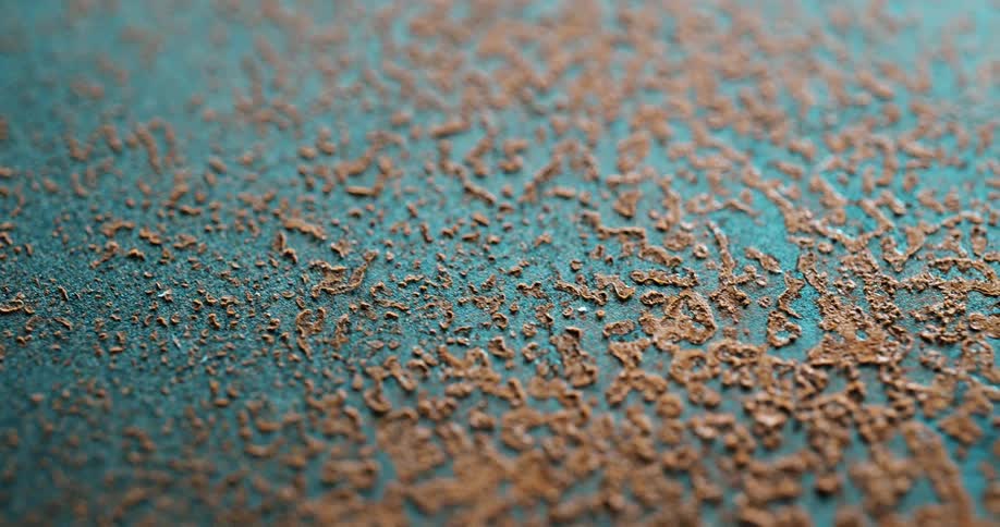A textured rust like pattern of brown corrosion spreads unevenly across a tealblue surface in sharp macro focus