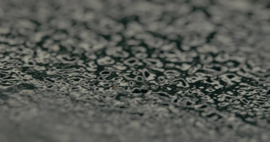Rippling water droplets form abstract patterns across a dark surface creating a mesmerizing texture in extreme close up