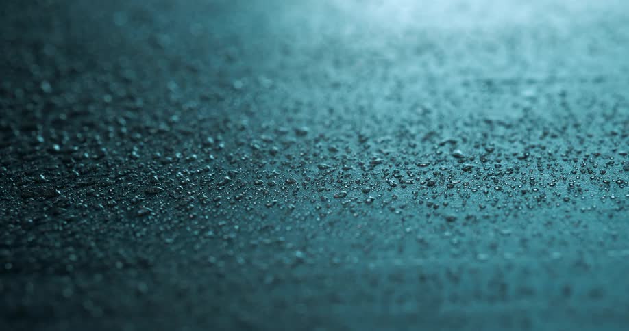 A macro shot of water droplets scattered across a smooth dark surface under cool blue lighting