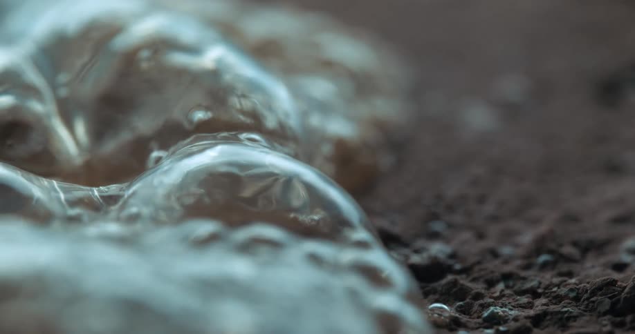 Bubbling liquid slowly expands on a textured surface captured in extreme closeup with high detail
