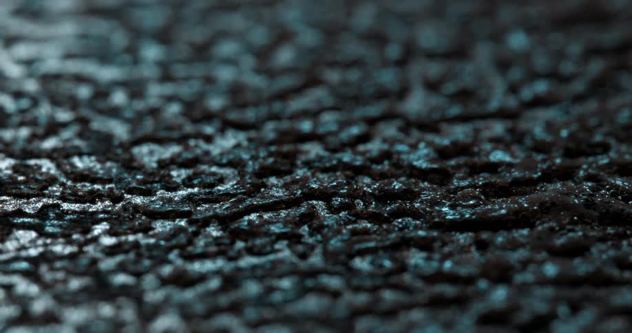 Dark surface with rough texture is seen in closeup with bluish lighting