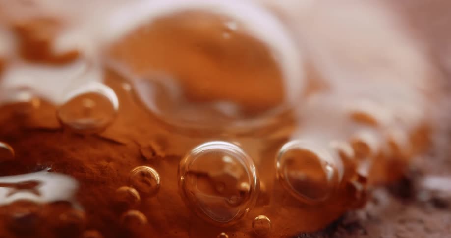 Translucent bubbles cluster on a warm amber surface forming a rich macro texture with vivid reflections