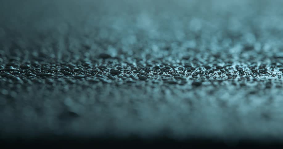 A macro shot of glistening water droplets on a textured surface bathed in cool blue lighting creating a serene and abstract visual