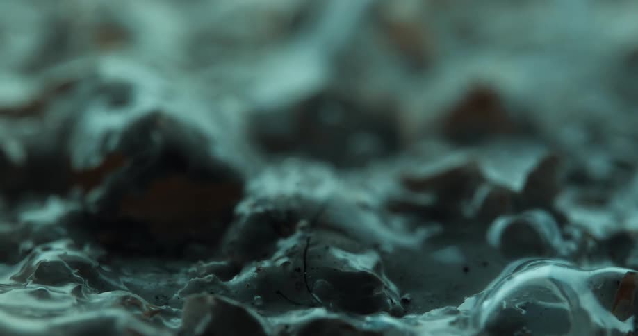 Bubbles form and distort the surrounding liquid surface creating a surreal abstract texture in soft bluegreen tones