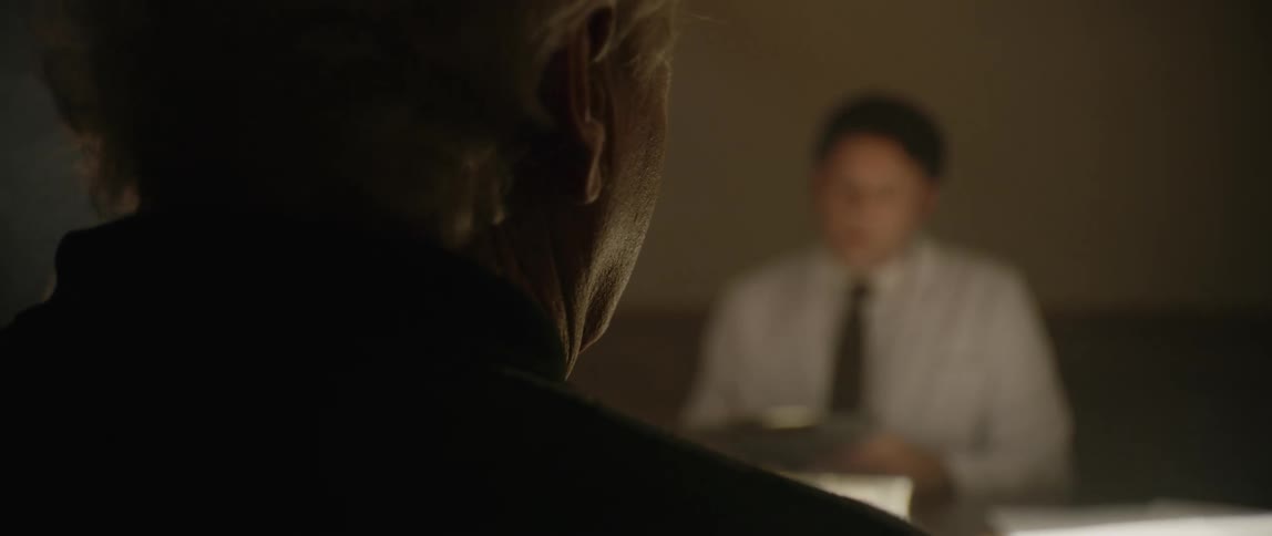 A man is seen in dramatic silhouette facing another man in focus possibly during an intense conversation or interrogation