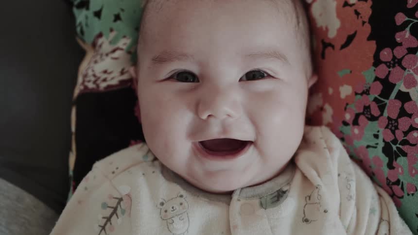 Baby lying against afloral patterned pillow smiles