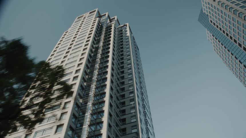 Tall modern skyscrapers with numerous windows are seen from a low angle against a clear blue sky