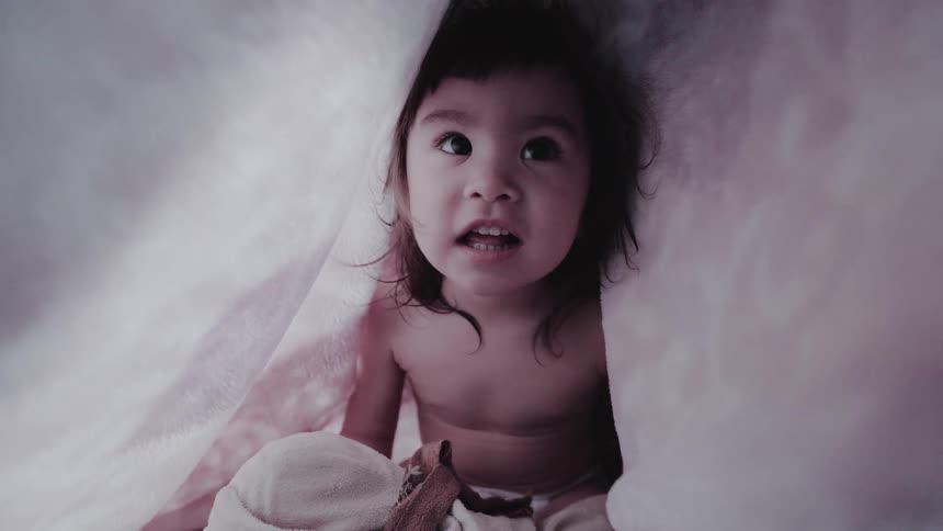 Toddler yells and laughs while playing hide and seek under a bed cover