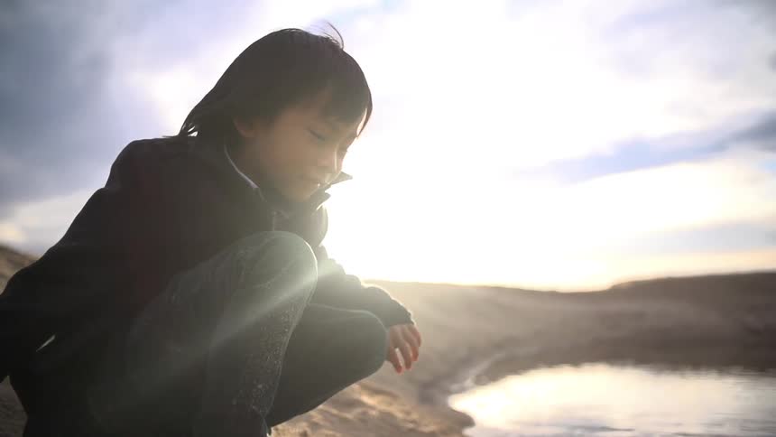 Small child throwing sand next to a small body of water