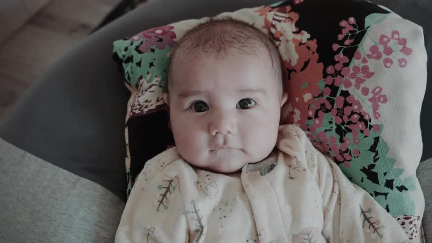 Baby lying on a cushion looks up into the camera