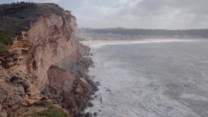 Waves roll in to shore and splash against rocks at the foot of a cliff