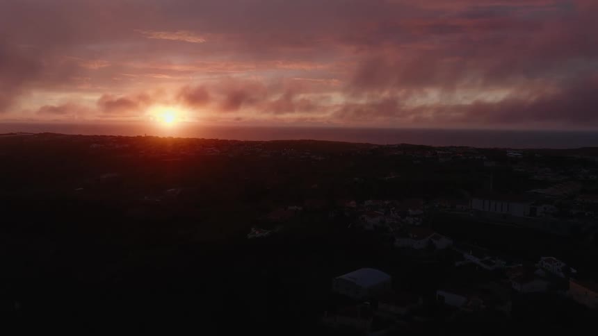 A vibrant sunset paints the sky with hues of orange and pink illuminating a dark silhouetted landscape