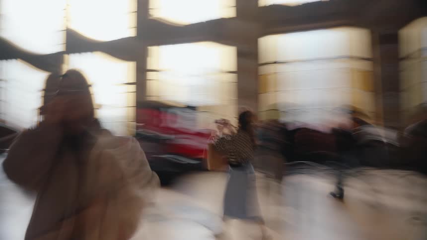 Blurry people walk while either carrying or moving bags on carts in the foyer of a transport terminal