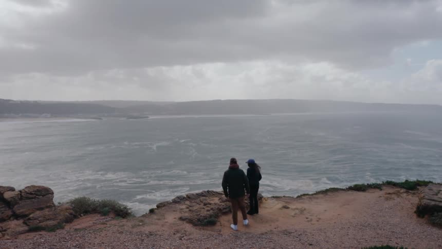 Two people watch the tide on the shore