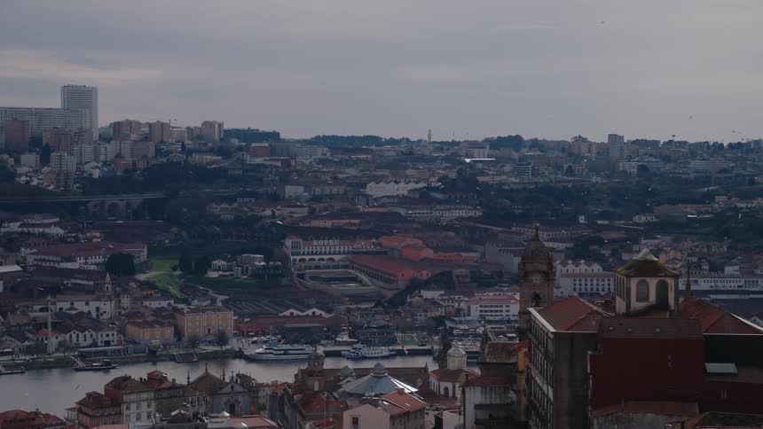 A city with old buildings and houses a church and a river running through it with many birds flying in the sky
