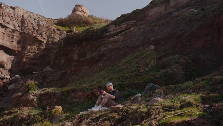 A man is reading a book while sitting on a mountain