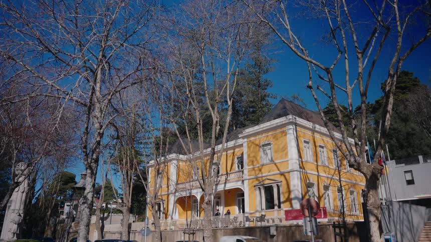 An old yellow mansion surrounded by trees with two people walking in front of it
