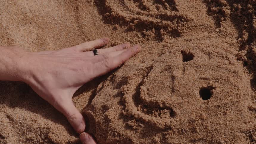 Hands of a man drawing a smiling face in the sand