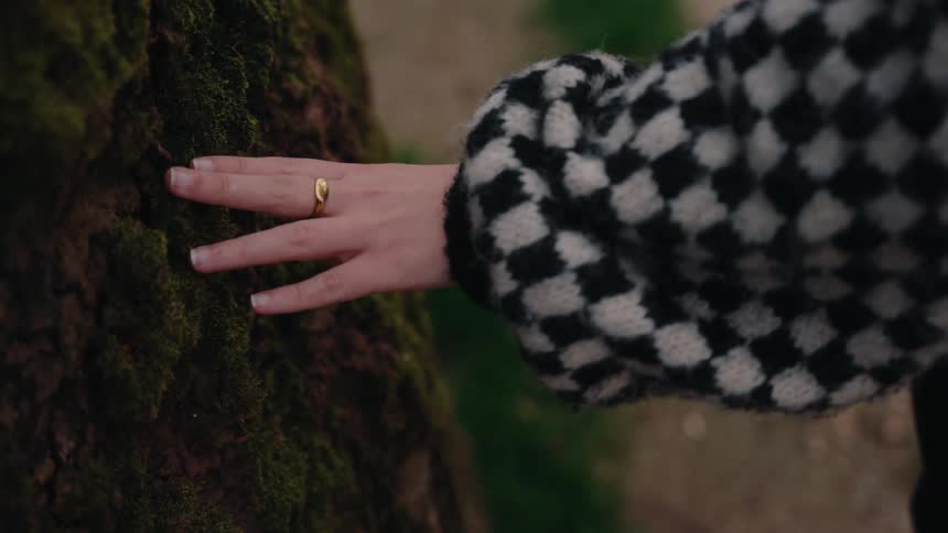 A woman places her hand on a tree trunk and walks away