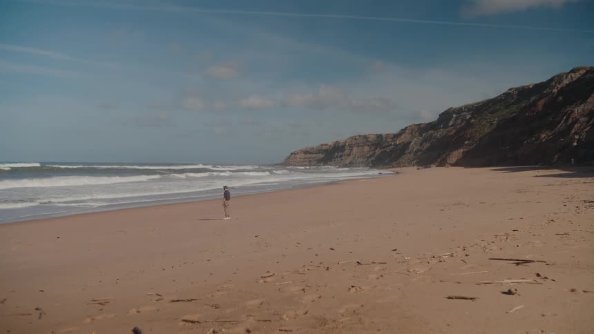 A man walks on the long beach and views the water