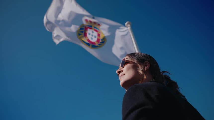 Woman standing in front of a flag waving in the wind under a blue sky