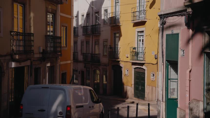 A narrow street in lisbon portugal showcases a white van driving between colorful buildings