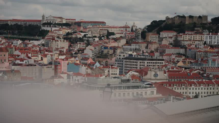 A cityscape of lisbon portugal shows a hilltop castle overlooking a sea of buildings