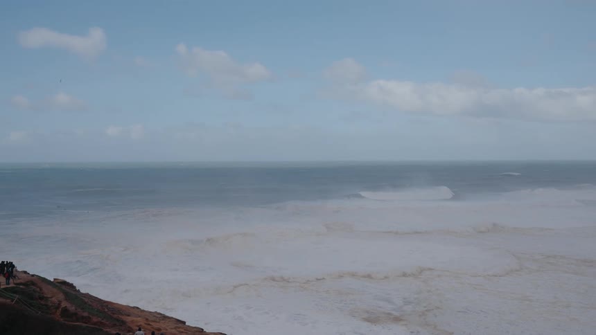A tumultuous sea churns with white foam extending to a distant horizon under a gray sky