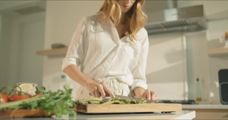 A woman is smiling while chopping vegetables in a bright modern kitchen