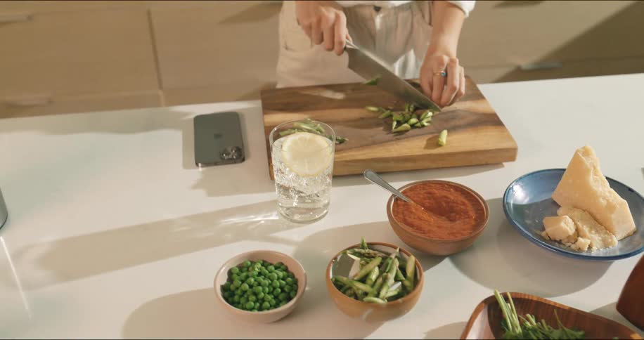 A woman is chopping vegetables then looks at her cellphone