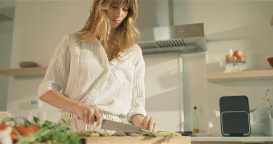 A woman is chopping vegetables in a well lit modern kitchen appearing focused and content