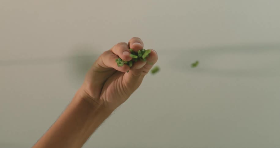 A hand is seen sprinkling fresh green herbs likely for cooking against a neutral indoor background