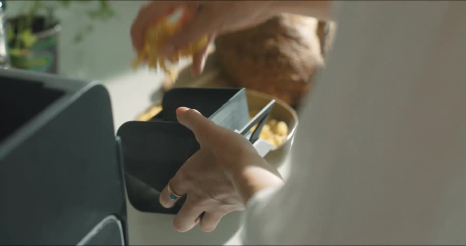 A woman puts dry spiral pasta into a square black container