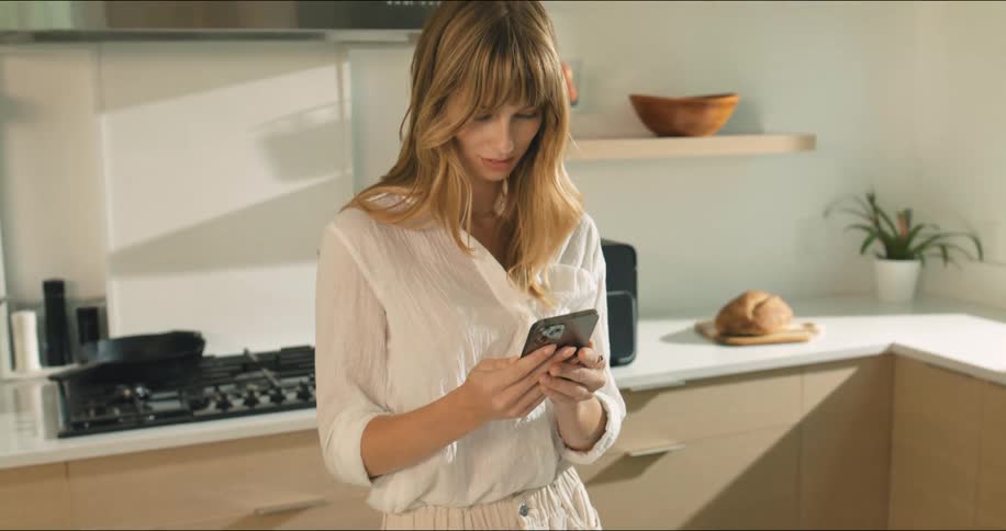 Woman with happy expression cooking and interacting with a smartphone