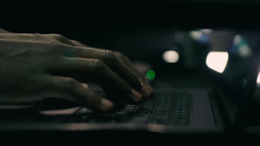 A person typing on their laptop in a dimly lit office