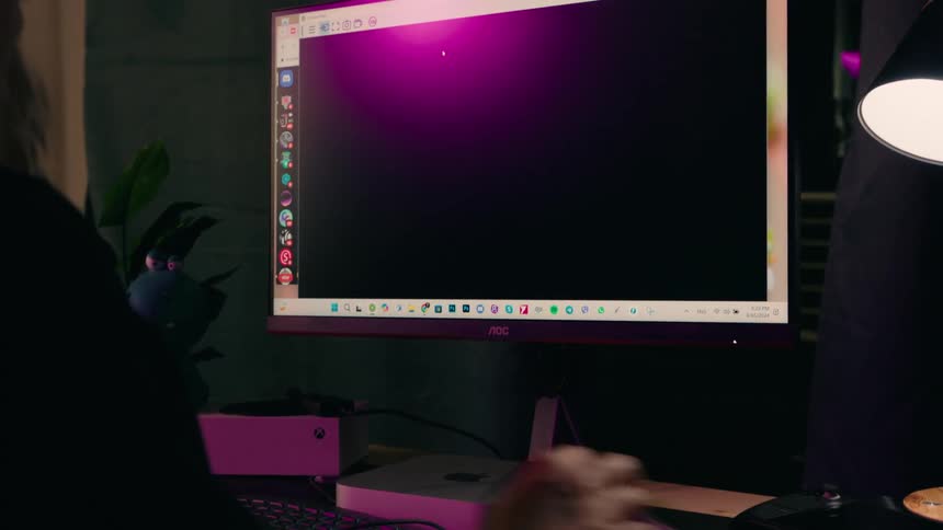 A person using a computer in a dimly lit room hand on a mouse screen showing a video call or stream