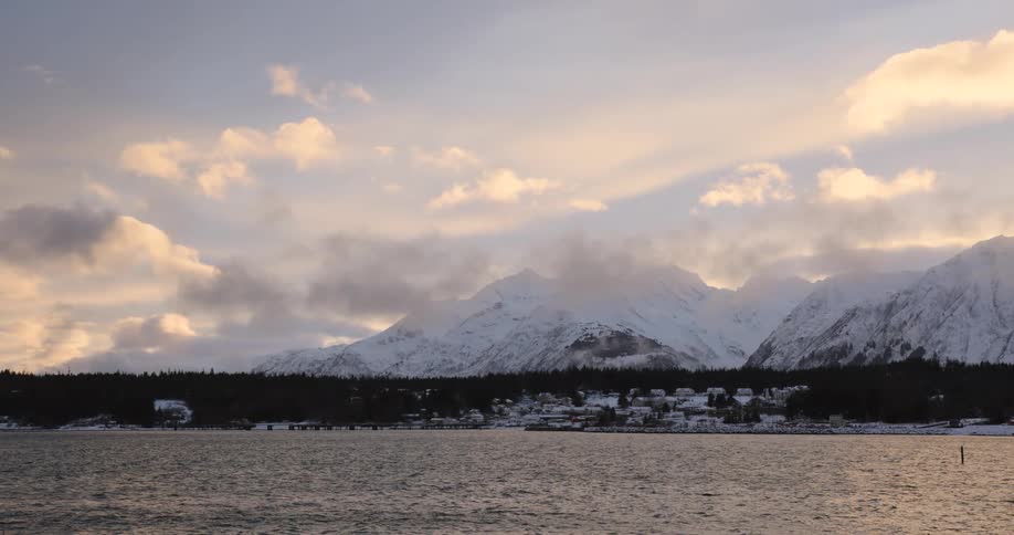 Small choppy waves hit the coast that has mountains covered in snow